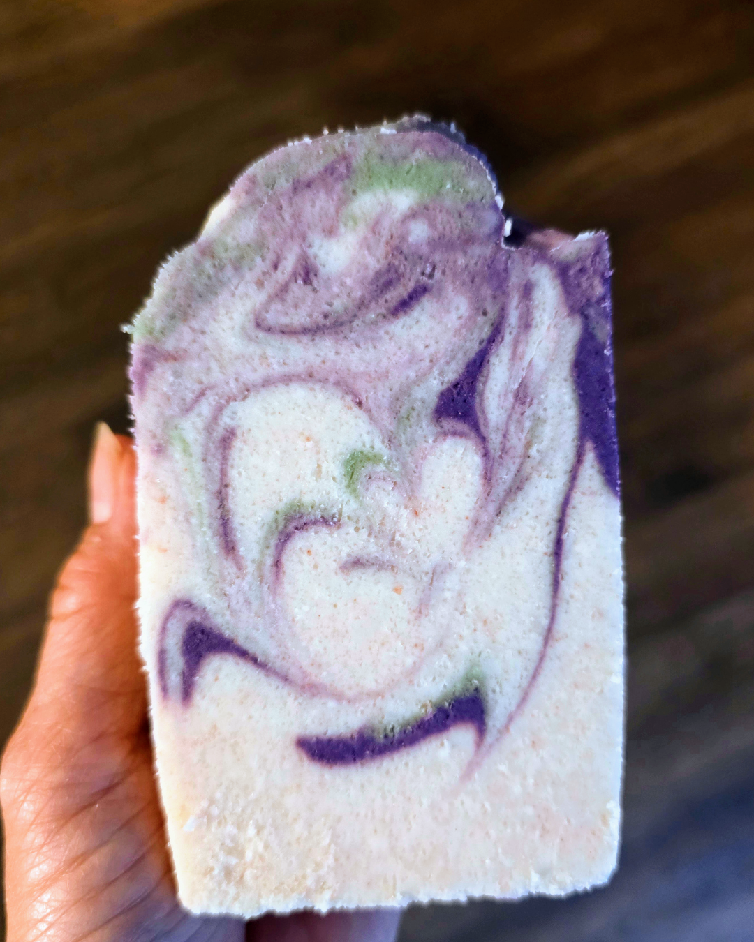 Dark purple, green and white swirled Salt bar. Hand holding Salt bar in backround.