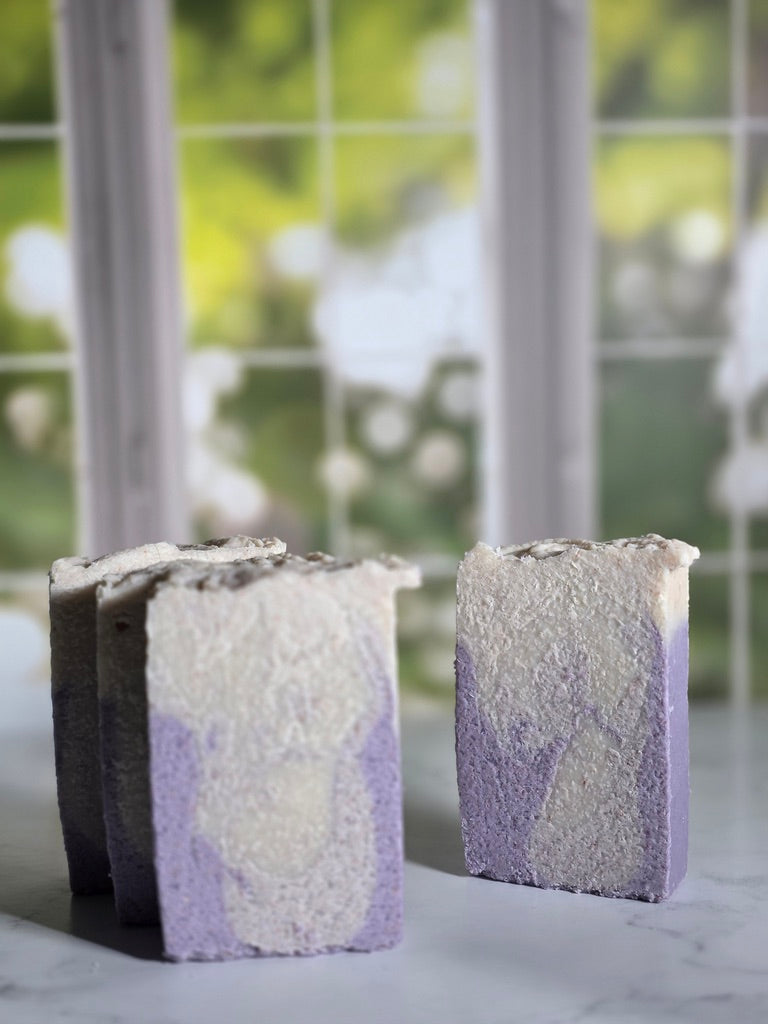 Four purple and white swirl Salt soap bars with a natural, textured surface on a marble surface.